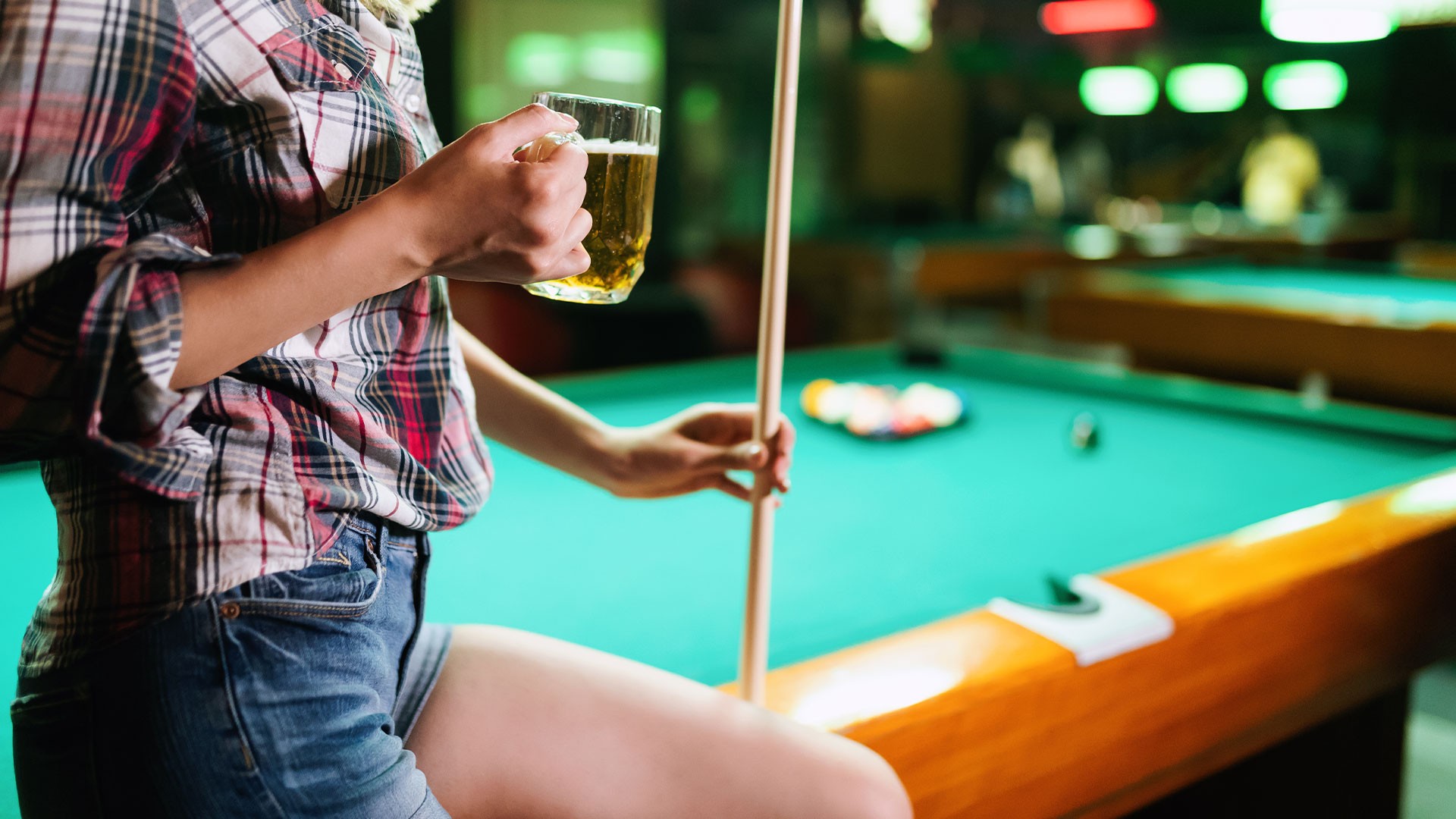 Bar patron holding a beer and a cue beside a pool table