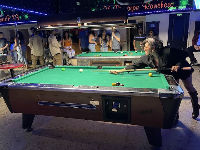 Player lining up a shot on a 7-foot coin-op table in a crowded bar